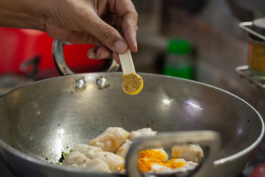 Indian woman adding turmeric to boiled taro root curry