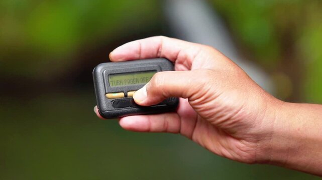 Hand holding pager beeper device, retro phone 90s instant communication and connection, sms messaging in the early 80s 90s digital age