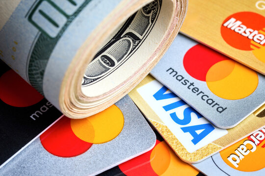 Berlin, Germany - July, 15 2026: finance concept, roll of US dollar banknotes lying over group of diverse visa and mastercard credit cards Cash and electronic payment methods for business transactions