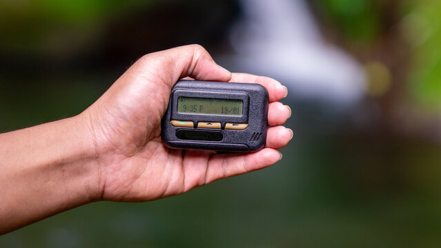 Hand holding pager beeper device, retro phone 90s instant communication and connection, sms messaging in the early 80s 90s digital age