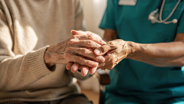 Close-up of elderly hands being held by a caregiver in teal scrubs, intimate gesture of support, concept for healthcare services, elder care and compassion advertising
