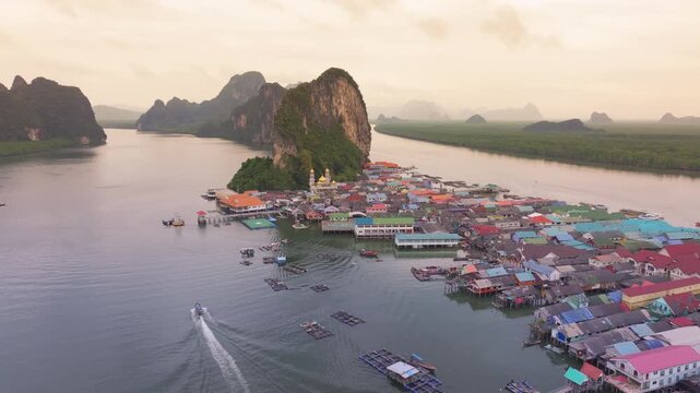 Aerial view showing the iconic Koh Panyi (Koh Panyee) fishing village built on stilts against a backdrop of limestone cliffs, lush mangroves, and a calm bay at dusk. Phang Nga, Thailand