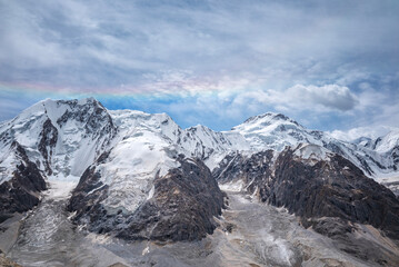 Obraz premium A stunning rainbow arches over the snow-capped peaks of the Tianshan Mountains in Xinjiang, China, creating a breathtaking natural spectacle against a dramatic sky.