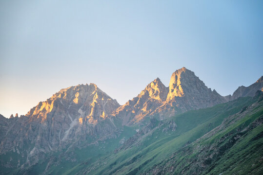 Golden sunlight illuminates the rugged mountain peaks of Ili River Valley, Xinjiang, China during a serene sunset