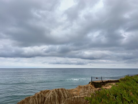 Gloomy summer morning overcast sky over coastal bluffs and safety fence overlooking the Pacific Ocean in Carlsbad, Southern California.