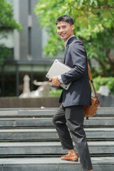 Obraz premium Asian businessman walking up stairs carrying laptop