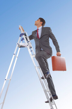 Businessman with suitcase climbing ladder