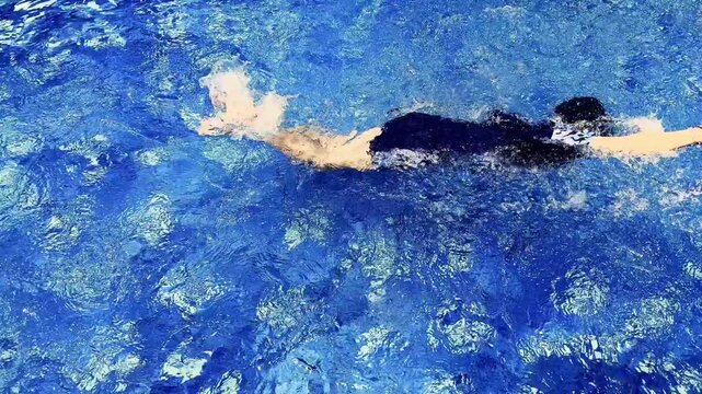 Clear blue pool water shimmers above submerged stones in bright natural sunlight.