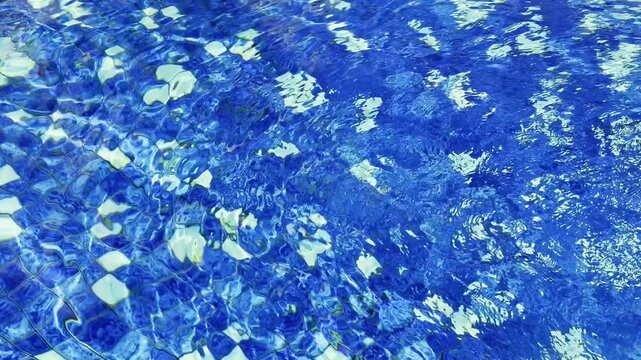 Sunlit ripples create vivid abstract patterns across clear blue swimming pool water.