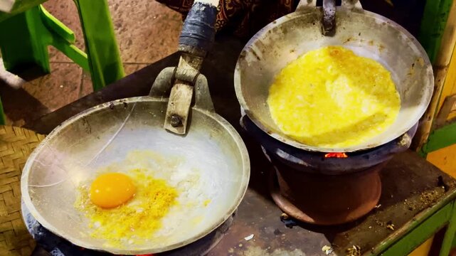 Cook prepares a golden omelet in metal pans over glowing charcoal flames.
