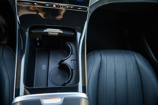 Modern luxury car center console storage compartment with cupholders, wireless charging pad, and USB-C ports, close up.