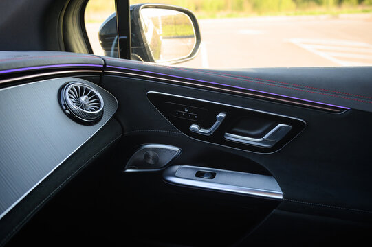 Passenger side interior door panel in a luxury car with an air vent, ambient lighting, and electric seat adjustment controls, close up.