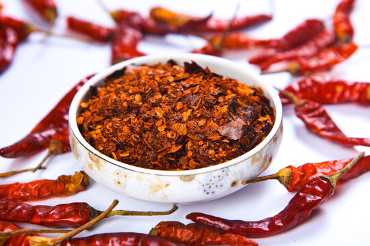 Crushed Red Chili Flakes In White Ceramic Bowl With Dried Peppers