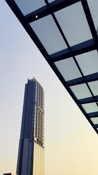 Modern skyscraper rises beside a geometric steel and glass canopy against a pale evening sky.