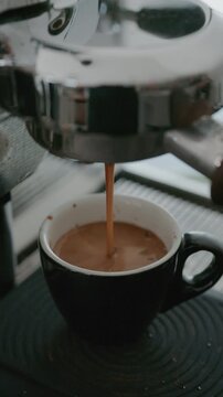 4K Pouring coffee stream from professional machine in cup. Barista man making double espresso, using filter holder. Flowing fresh ground coffee. Drinking roasted black coffee in the morning.
