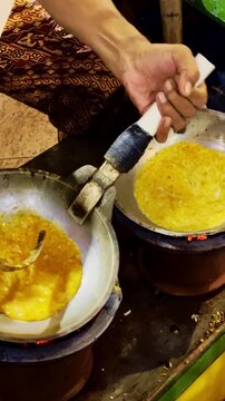 Cook seasons golden omelets frying in two pans over traditional charcoal stoves.