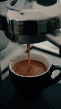 4K Pouring coffee stream from professional machine in cup. Barista man making double espresso, using filter holder. Flowing fresh ground coffee. Drinking roasted black coffee in the morning.
