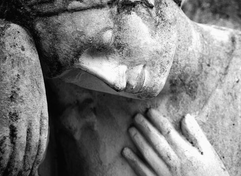 Black and white close-up of a grieving stone angel with bowed head and hand over the heart, symbolizing sorrow, loss, remembrance, compassion, and eternal peace.