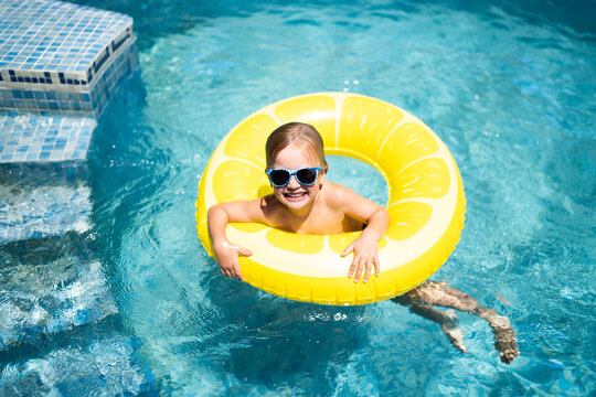 Blonde boy smiling in pool on lemon float with sunglasses