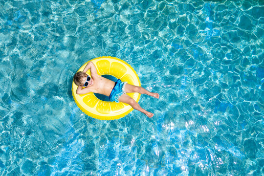 Blonde boy chilling pool lemon float sunglasses drone view
