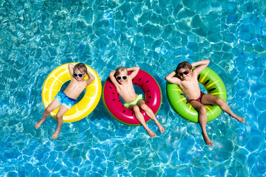 Drone view of 3 children chilling in pool on fruit floats sunglasses