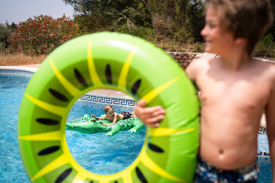 Young kid on crocodile floatie in pool through a ring floatie