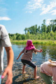 Young child stands barefoot in shallow river to skips rocks.