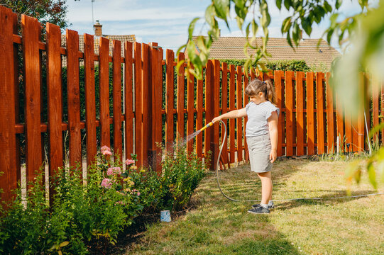 Child girl watering flowering plants in a sunny backyard garden