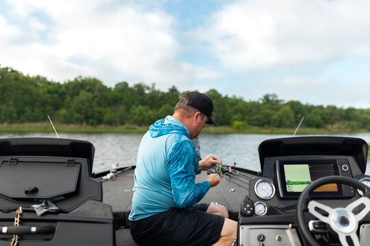 Man sits on bass boat preparing fishing lure