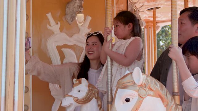 Happy Asian Family Taking Selfie While Riding Carousel Horses