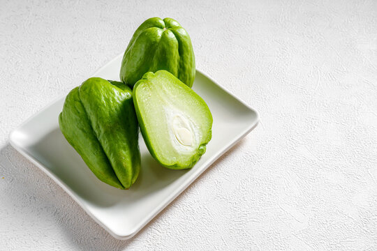 Halved fresh chayote squash with two whole chayotes on a table with wide copy space