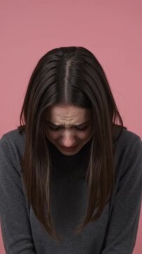 Brunette woman stands in front of pink background with tears in her eyes and sadness on her face