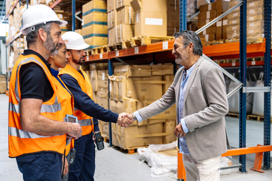 Diverse team of logistics workers and a manager shaking hands, collaborating in a distribution center