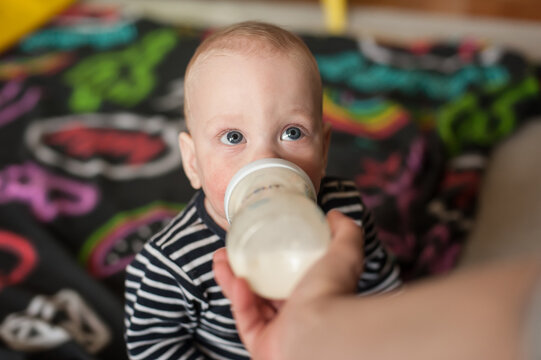A sweet baby boy in a striped shirt enjoys a peaceful morning bottle, gazing up with wide blue eyes