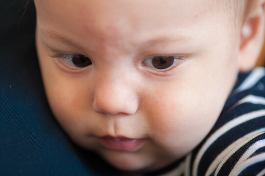 Deep wonder shines in the curious dark eyes of a tiny infant resting peacefully on a parent shoulder during a quiet afternoon at home