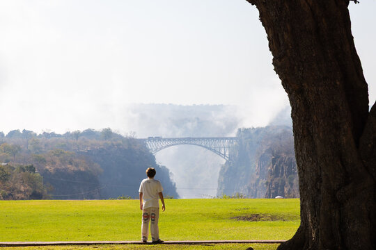 young boy walking past view of Victoria Falls and Victoria Falls Bridge from the Zimbabwe side, Zimbabwe, Africa