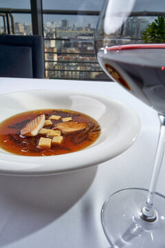 Gourmet mushroom consomme soup with grilled king oyster mushrooms, croutons, and a glass of mint water on a sunny restaurant table.
