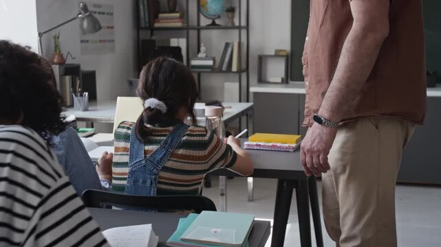 Tilt down shot of mature Caucasian male teacher walking through classroom and guiding African American teenage student with supportive gesture. Clip for school marketing and educational promos