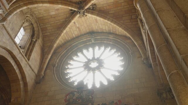 Light streams through an ornate rose window high above the nave of a medieval stone cathedral.
