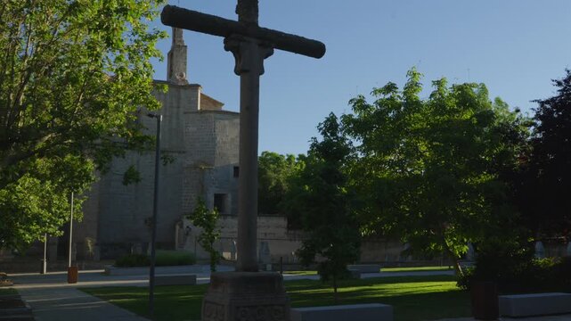 A historic stone wayside cross stands before ancient medieval walls in a timeless outdoor setting.