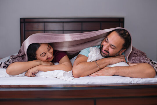 Smiling Couple lying together under blanket on bed 