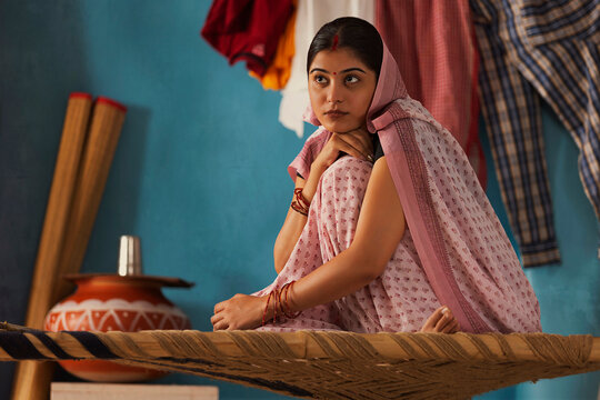 Portrait of housewife sitting on cot with resting her chin on knee