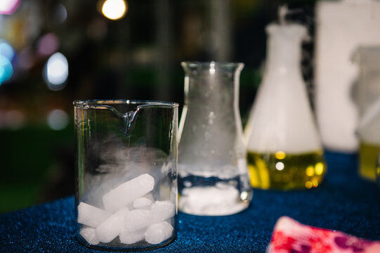 Close-up of glass laboratory beakers and flasks with dry ice pellets, water, and chemical reactions creating smoke for a children's science show.