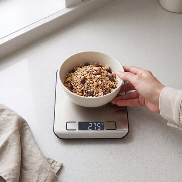 Hand placing a bowl of granola mix on a digital scale reading 275 grams