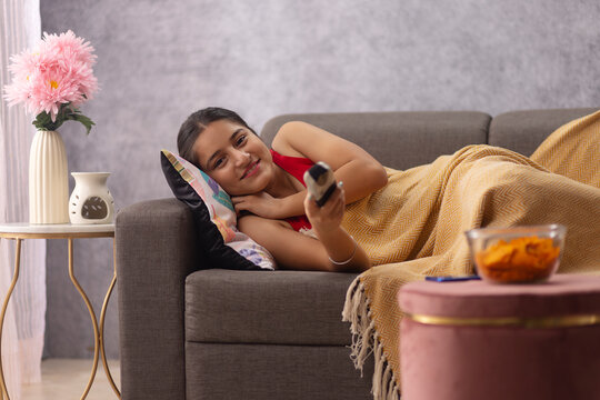 Teenage girl watching TV while lying on sofa at home