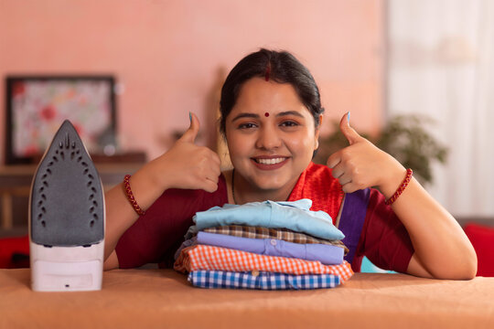 Close-up portrait of a happy woman showing thumbs up next to ironed shirts