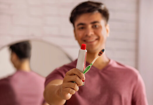 Young man holding toothbrush and toothpaste in bathroom