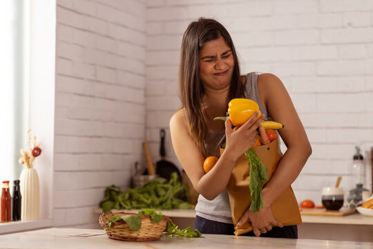 Woman standing in kitchen holding a heavy bag of vegetables