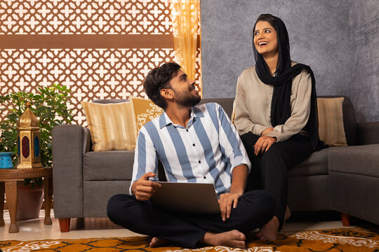 Happy Muslim couple using laptop in living room