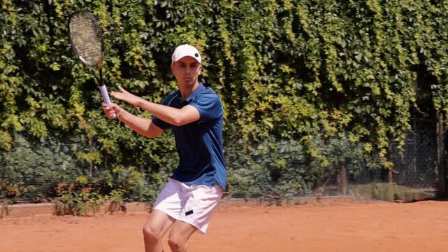 Male tennis player hitting two handed backhand on outdoor clay court during match. Concept of tennis training, athletic performance, competitive sport, focus, precision and active lifestyle.